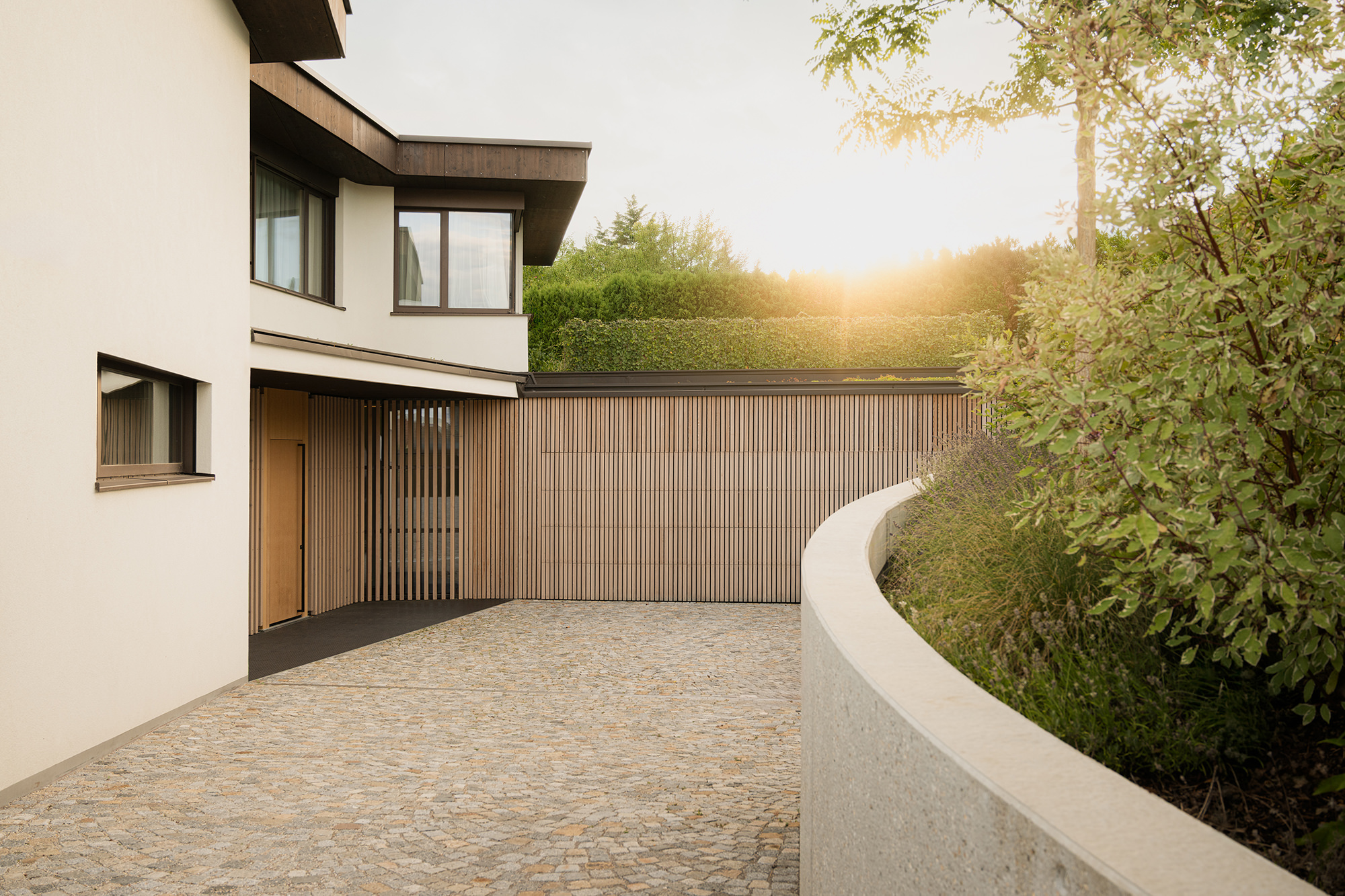 Gebogene Einfahrt aus Pflastersteinen und einer mit Holz verkleideten Garage