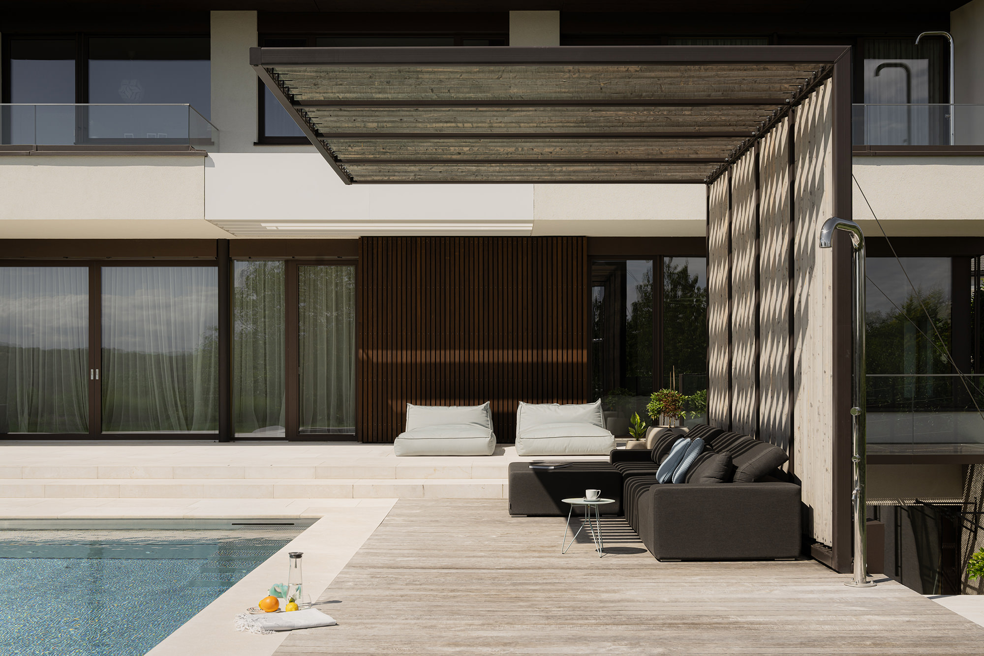 Nahaufnahme des überdachten Lounge Bereichs neben dem Outdoor Pool, davor eine Outdoor Dusche