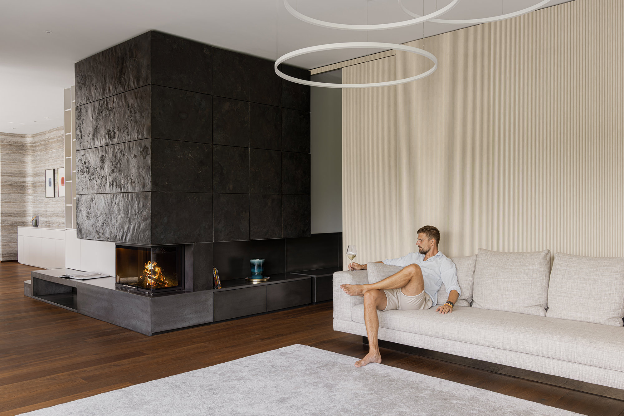 Wohnbereich mit großem, zentralen Kamin neben dem ein Mann mit einem Glas Weißwein auf dem Sofa sitzt