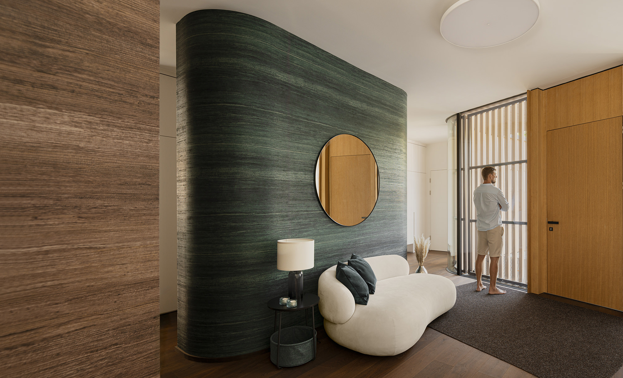 Eingangsbereich mit Blick zur Eingangstüre neben der ein Mann durch die große Glasfront, welche mit Holstäben verdunkelt wurde, nach draußen blickt