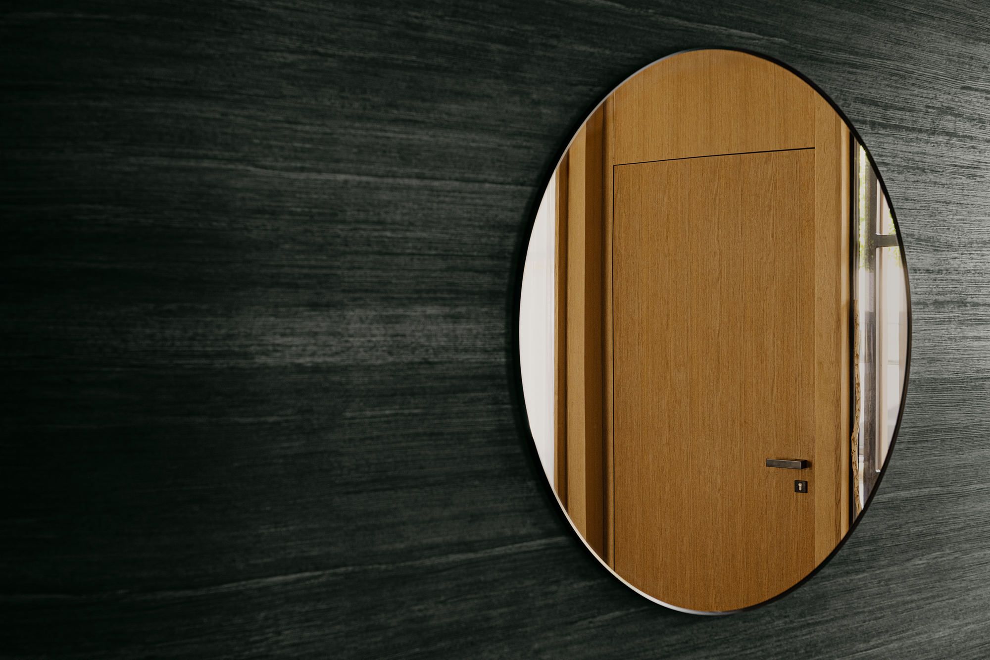 Großer runder Spiegel im Eingangsbereich welche eine Türe in Hintergrund reflektiert