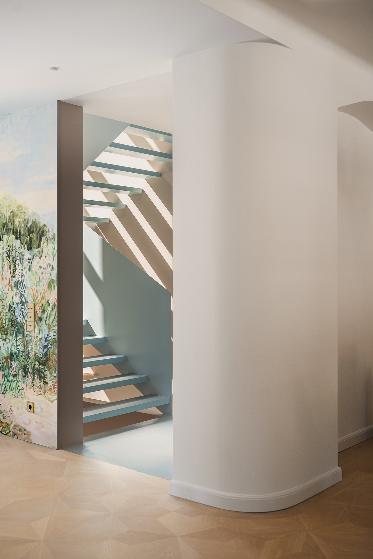 Blick auf den geschlossenen, aber in hellblau gehaltenen Treppenraum. Rechts eine abgerundete Ecke und links eine Wand mit Tapete auf der Pflanzen illustriert sind.