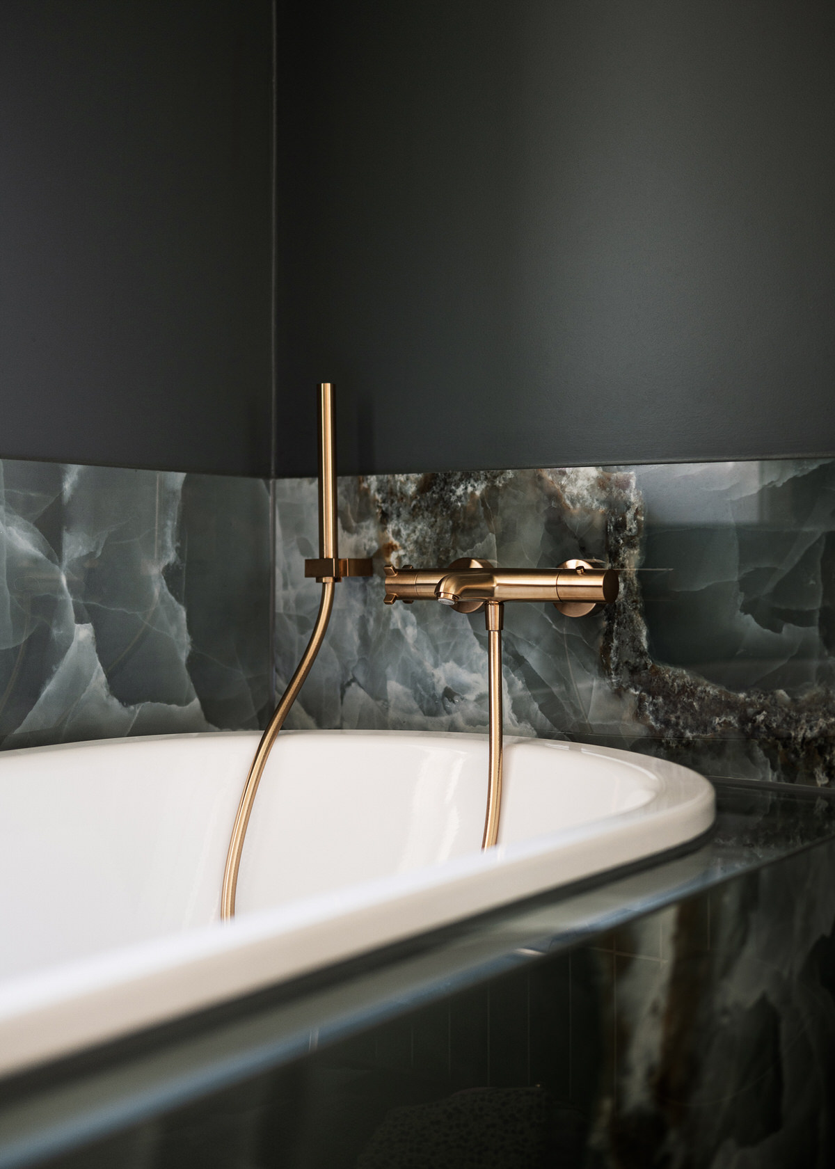 Nahaufnahme einer kupfernen Badewannenarmatur. Der Schlauch der Handbrause hängt in die Wanne, die außen mit Marmor verkleidet ist.