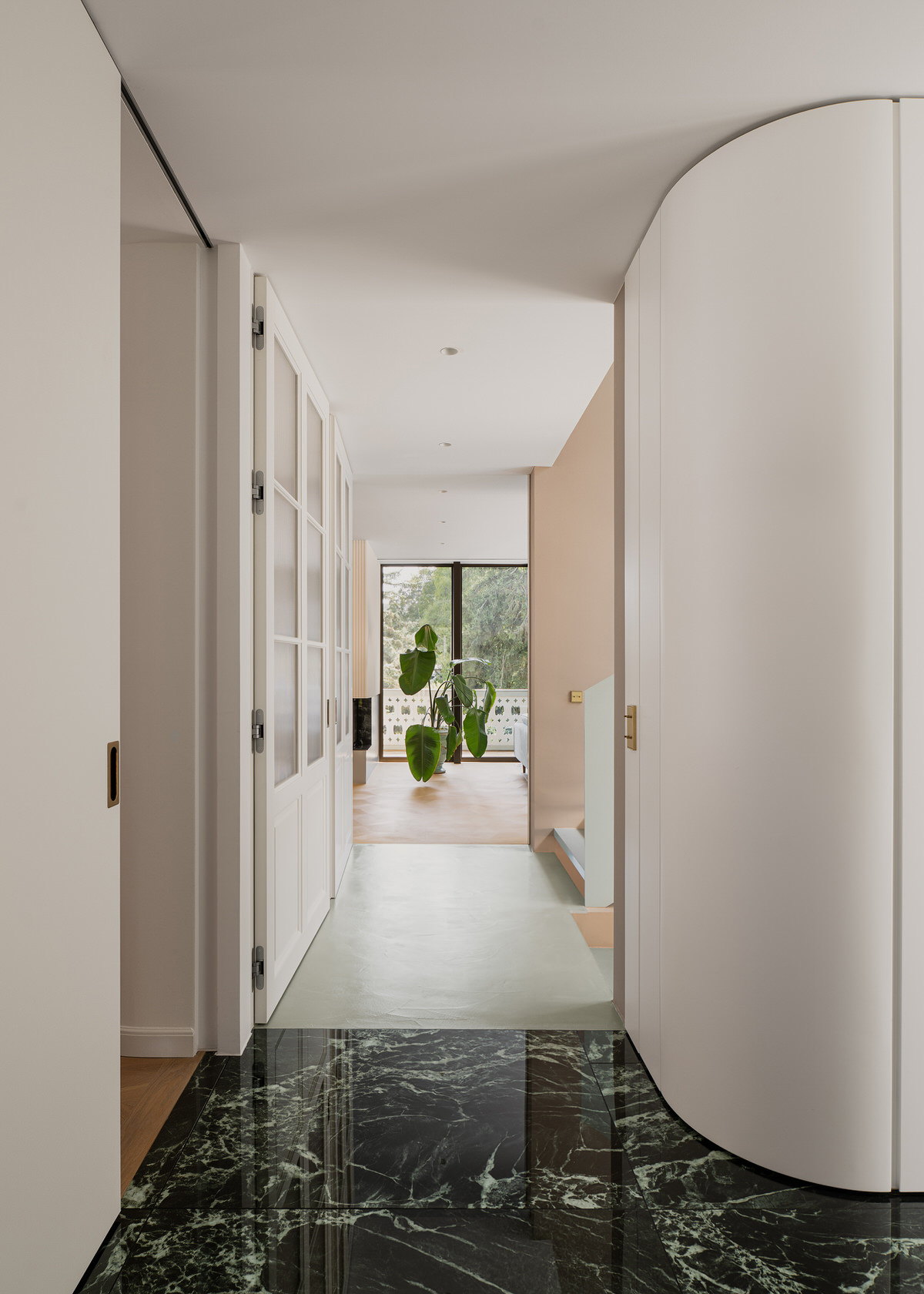 Blick durch den Treppenraum ins Wohnzimmer, wobei drei unterschiedliche Bodenbeläge der durchlaufenden Räume sichtbar sind.