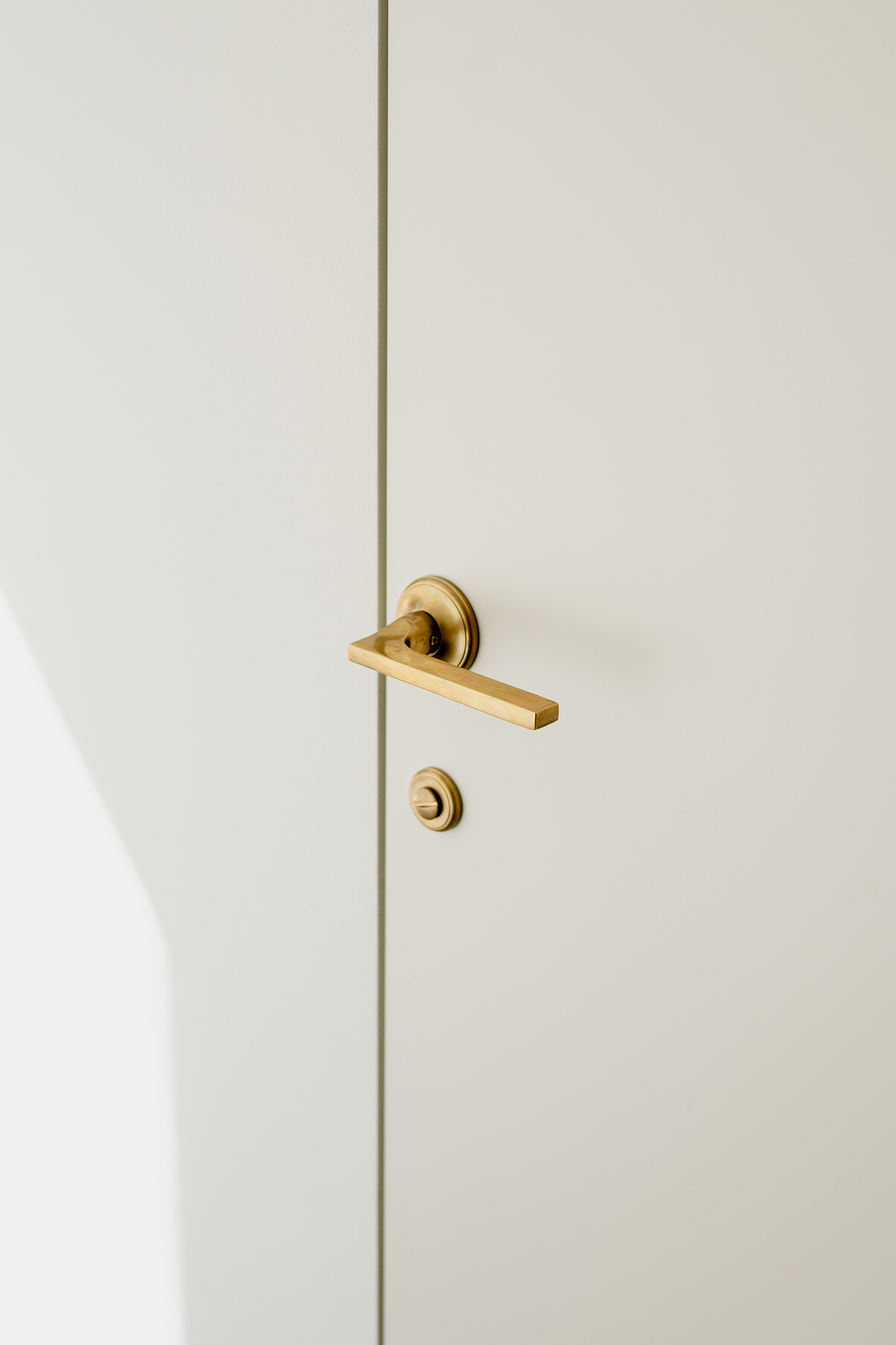 Nahaufnahme einer Messing-Türklinke. Die weiße Tür schließt bündig, sodass keine hervorstehenden Kanten sichtbar sind.