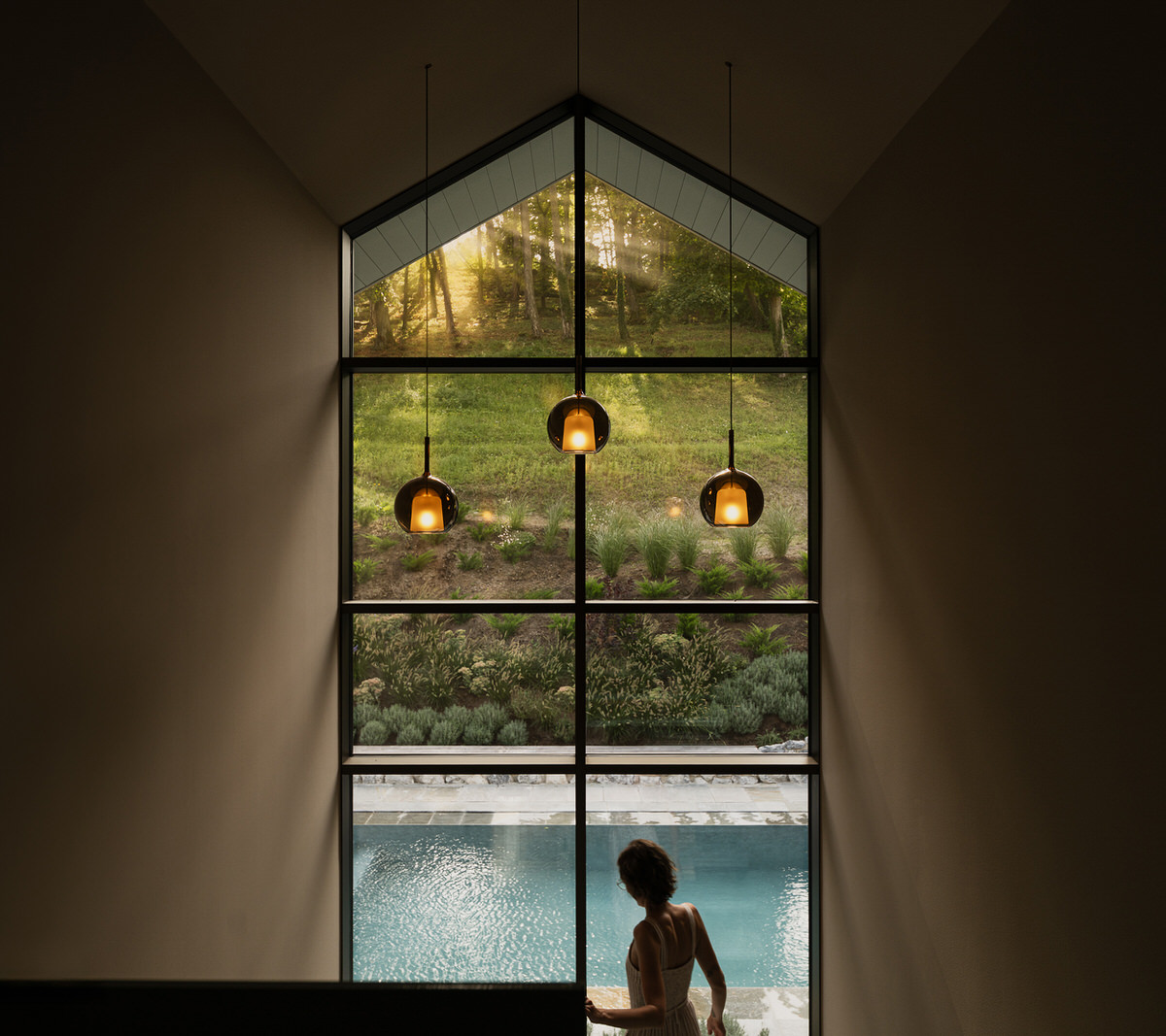 Eine Frau geht die Treppe hinunter. Vor ihr erstreckt sich eine bodenhohe Fensterfront mit Blick auf den Garten und den Pool.