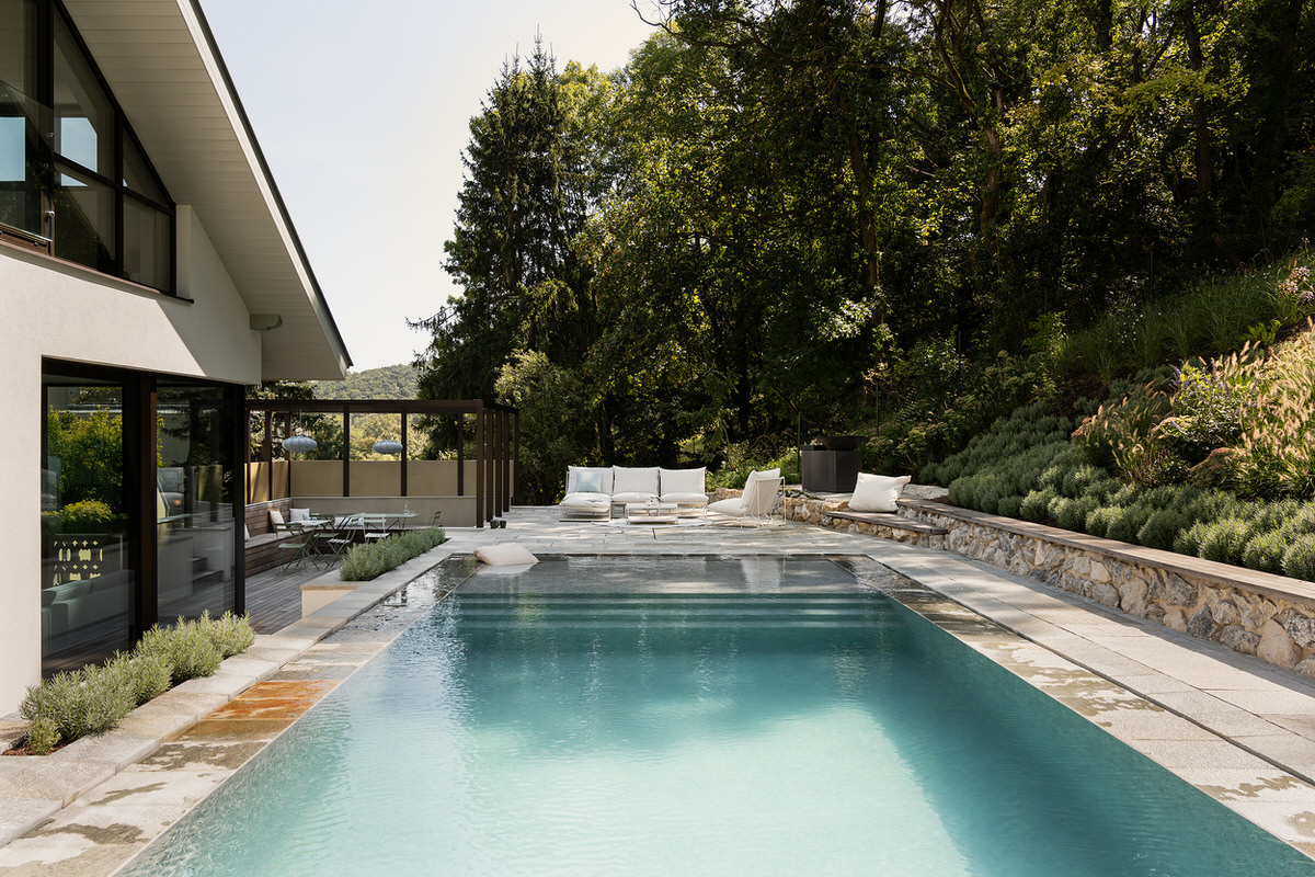 Blick auf den Pool mit einer weißen Sitzgelegenheit im Hintergrund. Links im Bild ist das Haus zu sehen.