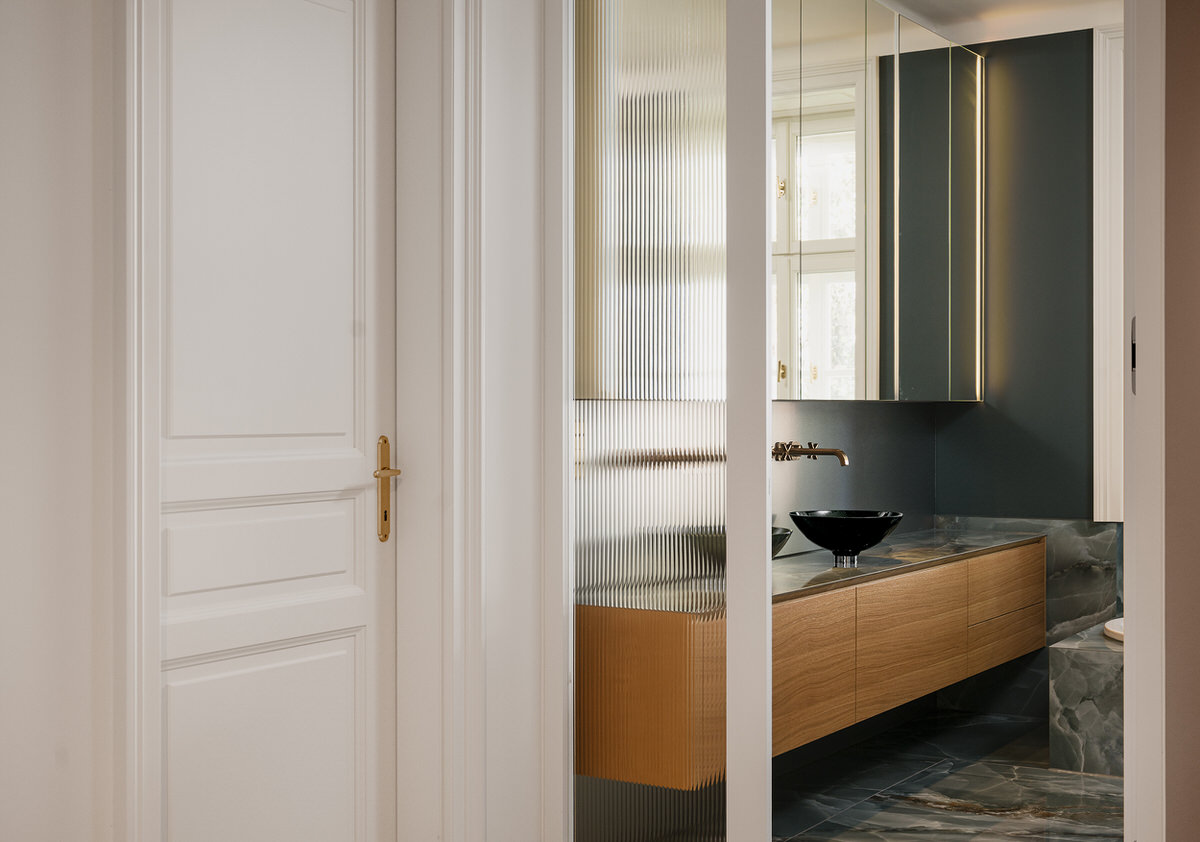 Blick auf ein kleines Waschbecken auf einem schwebenden Unterschrank mit großer Spiegelfront darüber. Im Vordergrund steht eine Tür.