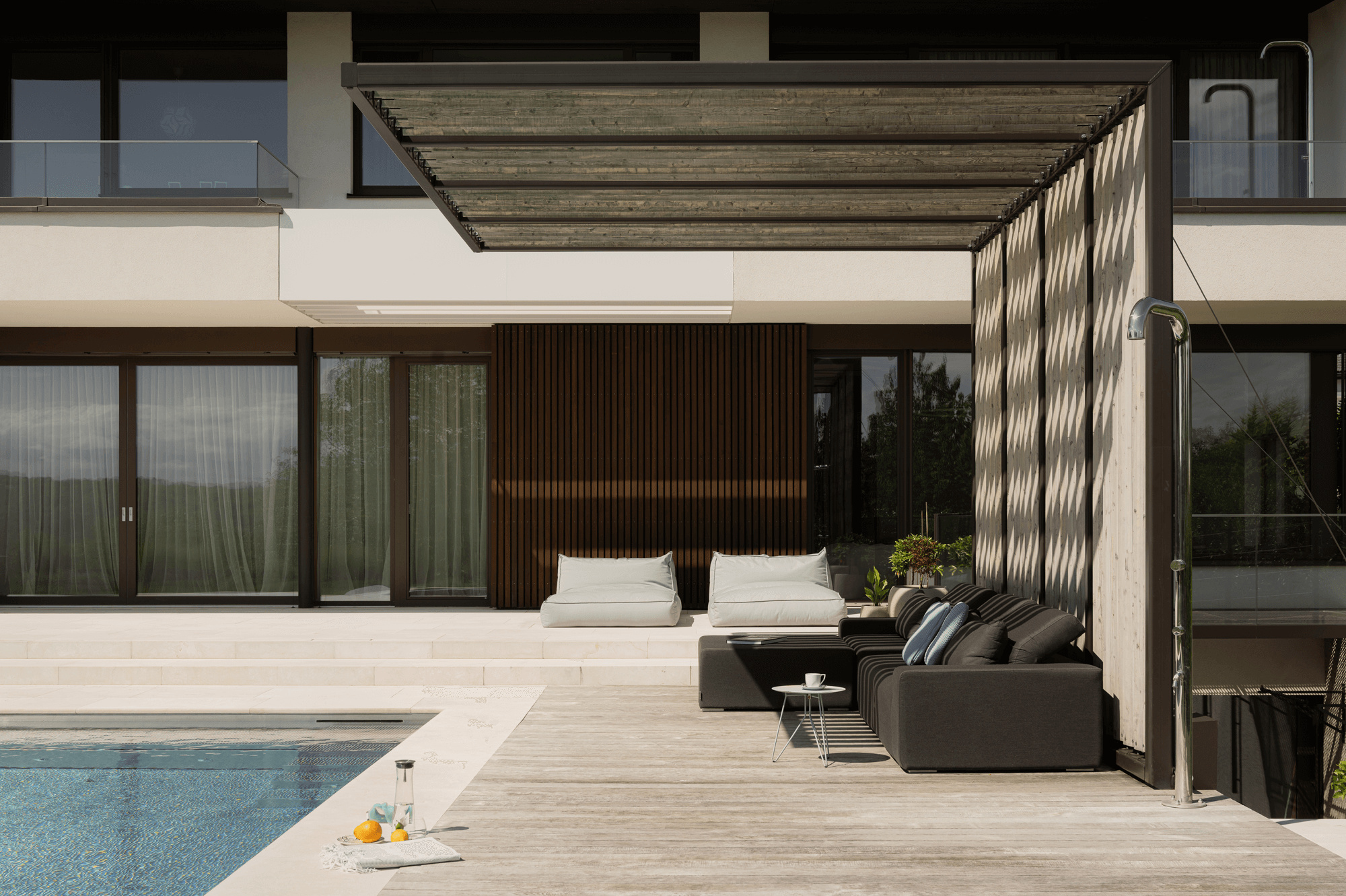 Nahaufnahme des überdachten Lounge Bereichs neben dem Outdoor Pool, davor eine Outdoor Dusche