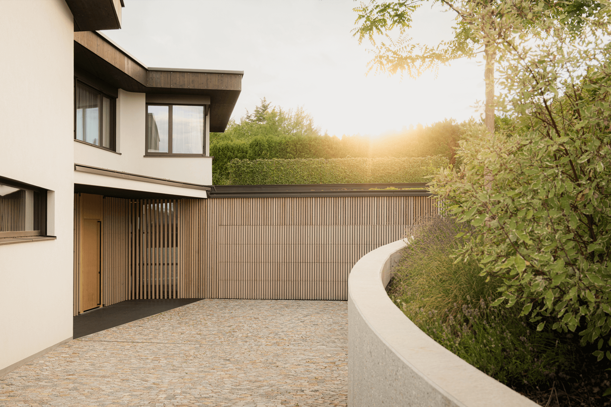 Gebogene Einfahrt aus Pflastersteinen und einer mit Holz verkleideten Garage