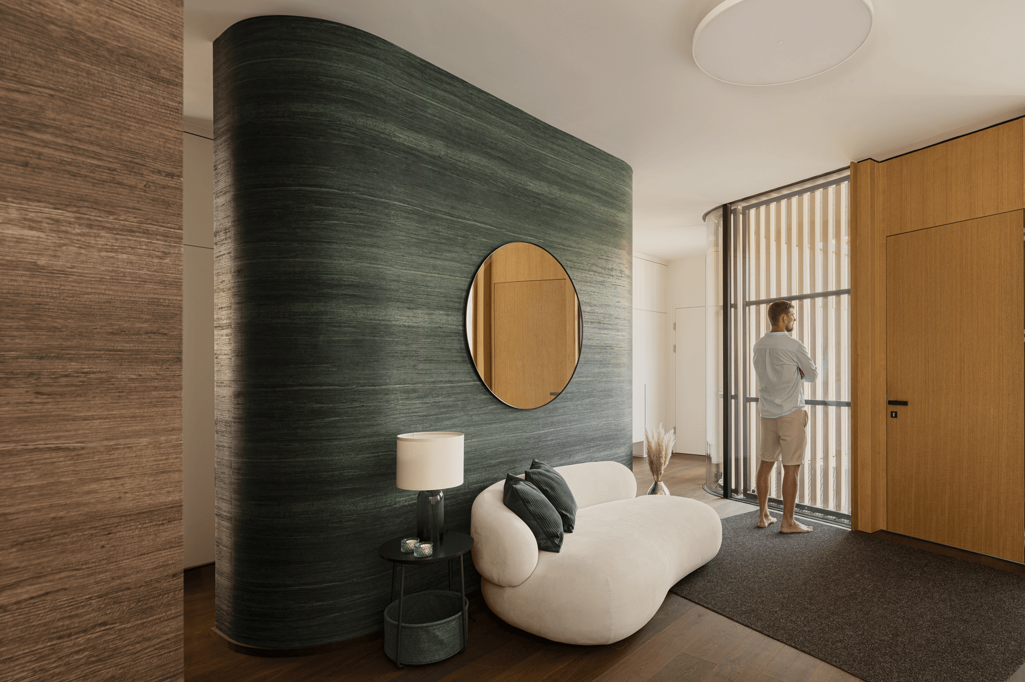 Eingangsbereich mit Blick zur Eingangstüre neben der ein Mann durch die große Glasfront, welche mit Holstäben verdunkelt wurde, nach draußen blickt