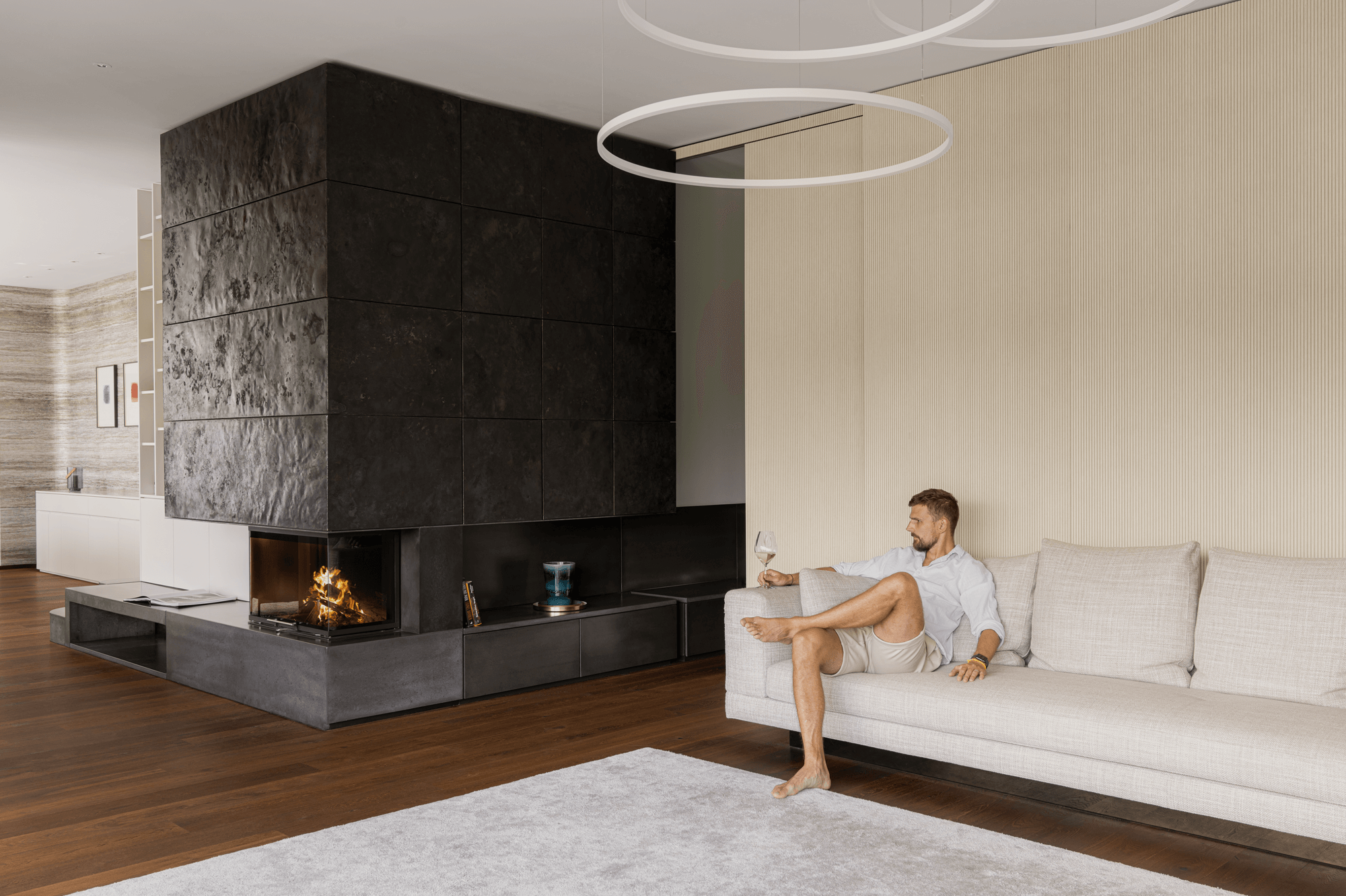 Wohnbereich mit großem, zentralen Kamin neben dem ein Mann mit einem Glas Weißwein auf dem Sofa sitzt
