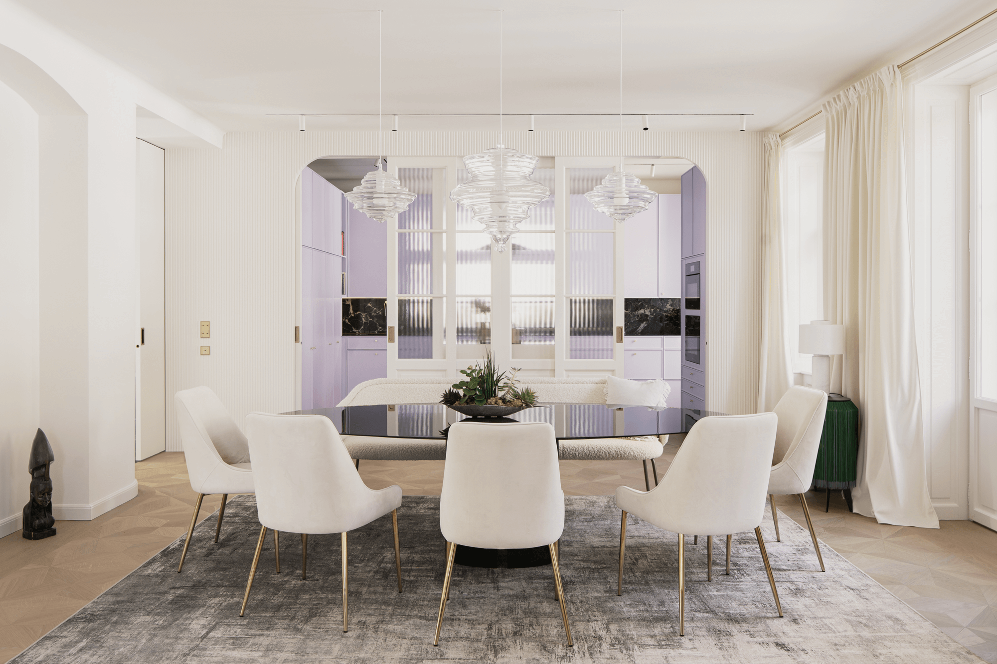 Hell gestaltetes Esszimmer mit ovalem Esstisch. Dahinter befindet sich die Küche, welche durch ihre lila Farbe deutlich hervorsticht.