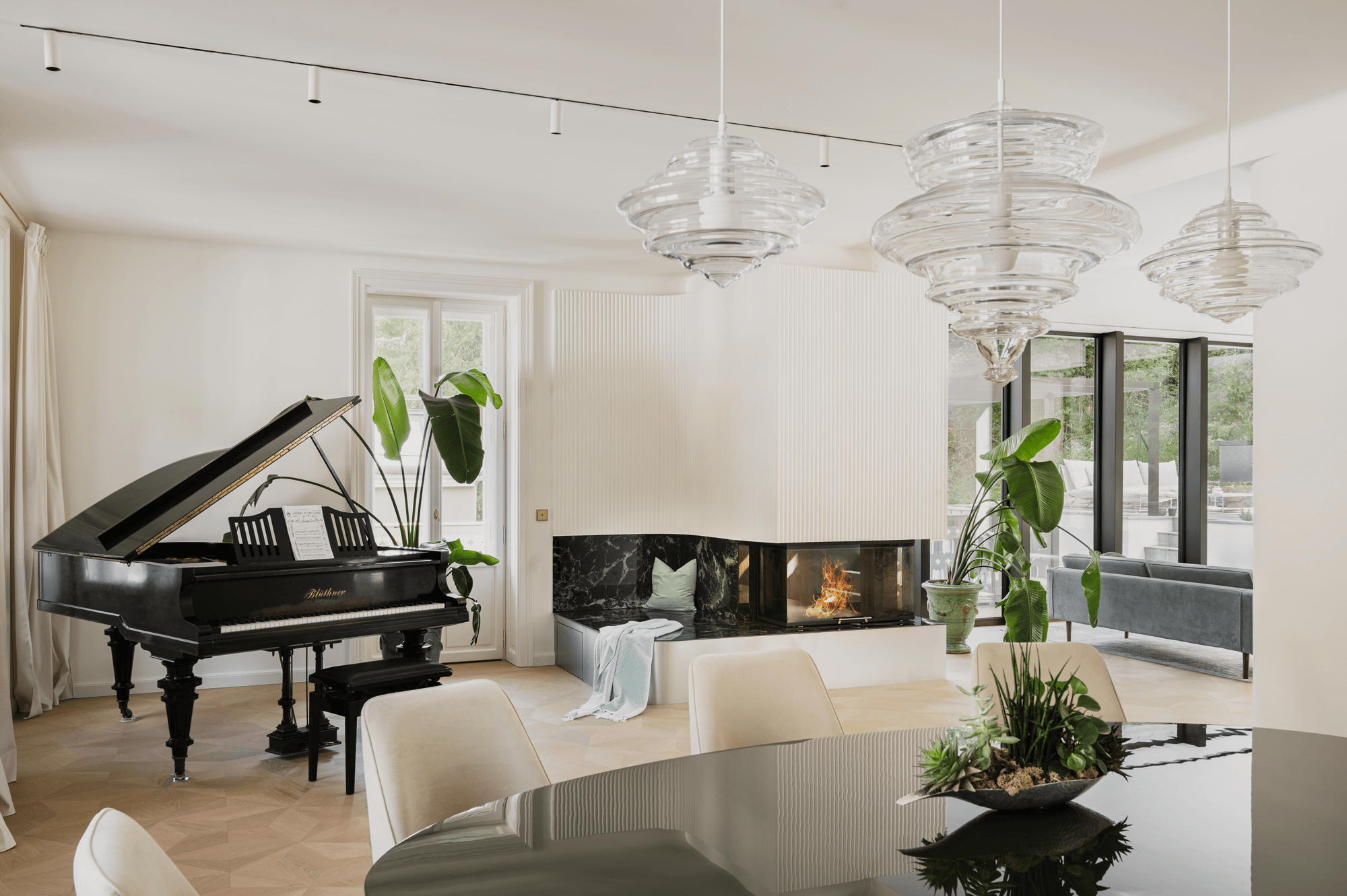 Blick vom Esszimmer auf einen geöffneten schwarzen Flügel links im Raum. In der Mitte steht ein weiß verkleideter Kamin mit einer kleinen Sitzfläche aus Marmor. Rechts ist die Rückseite einer Couch zu sehen.