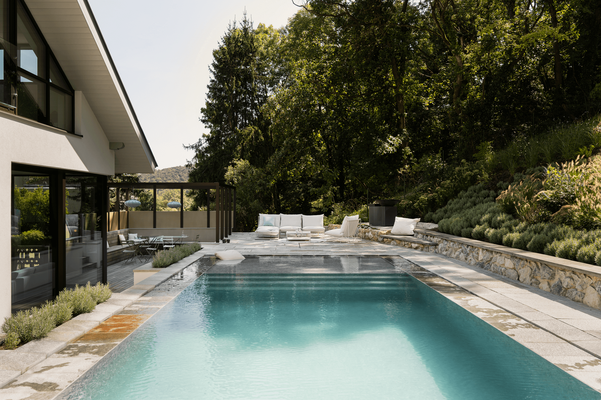 Blick auf den Pool mit einer weißen Sitzgelegenheit im Hintergrund. Links im Bild ist das Haus zu sehen.