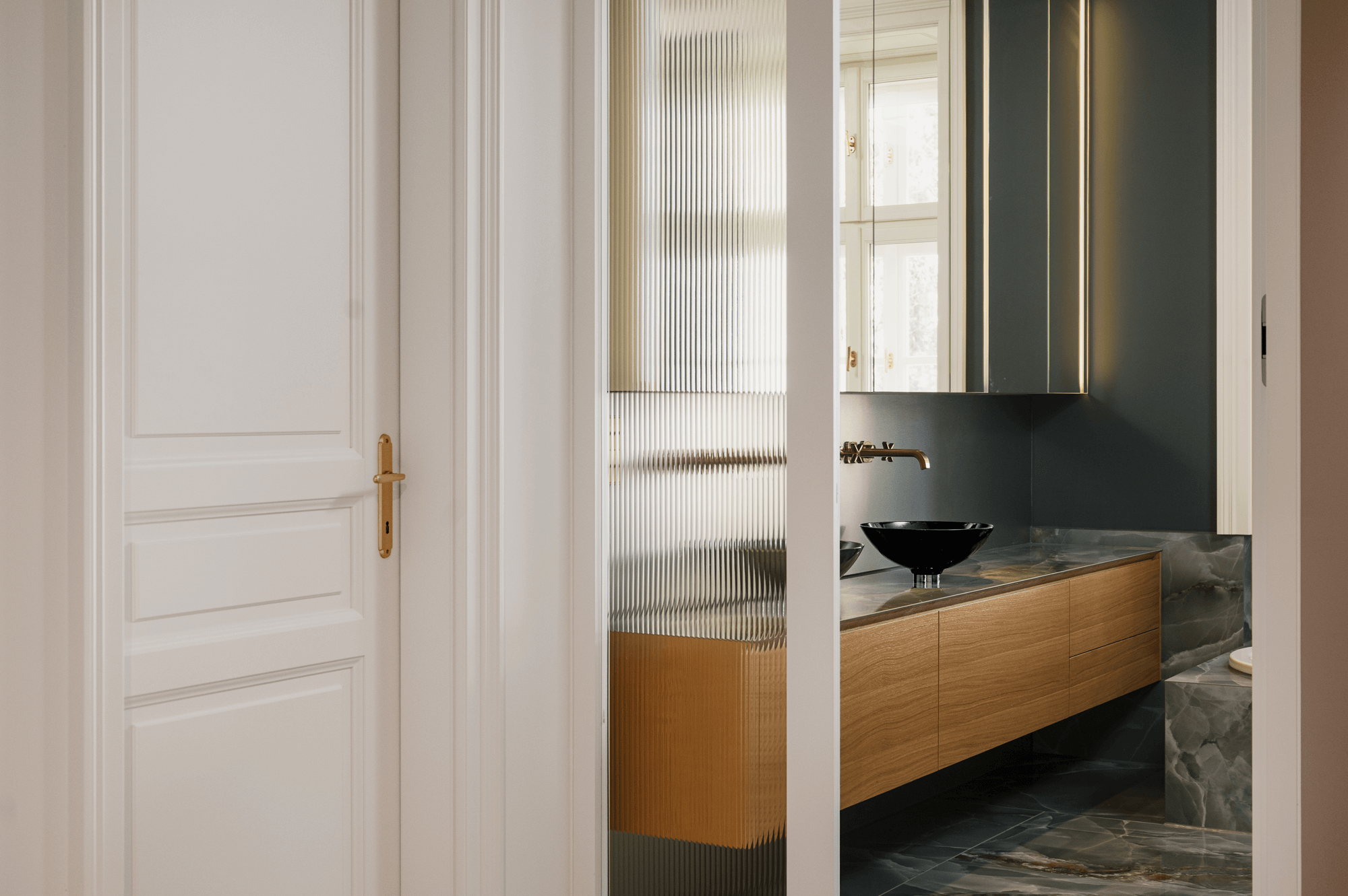 Blick auf ein kleines Waschbecken auf einem schwebenden Unterschrank mit großer Spiegelfront darüber. Im Vordergrund steht eine Tür.