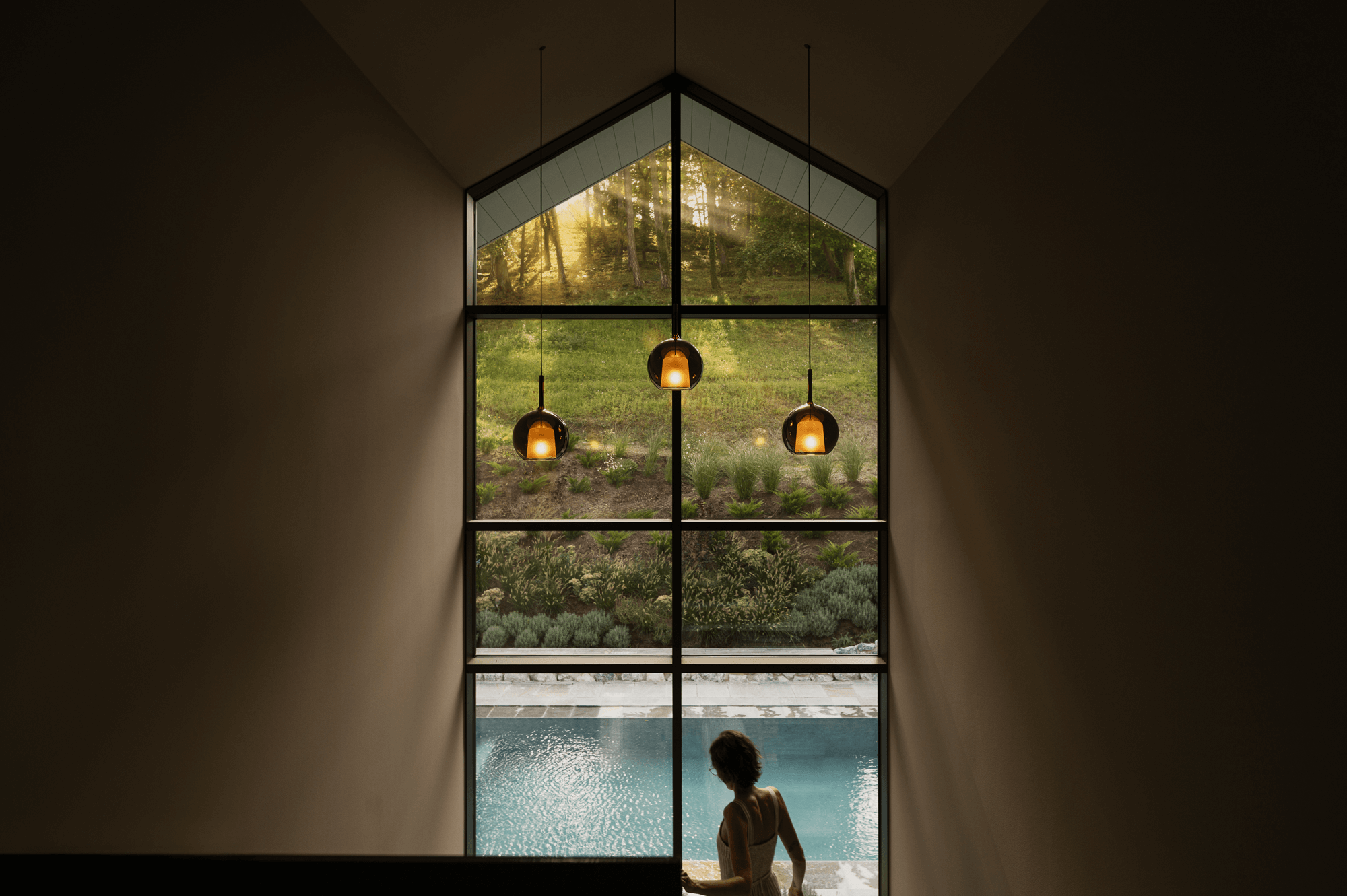 Eine Frau geht die Treppe hinunter. Vor ihr erstreckt sich eine bodenhohe Fensterfront mit Blick auf den Garten und den Pool.